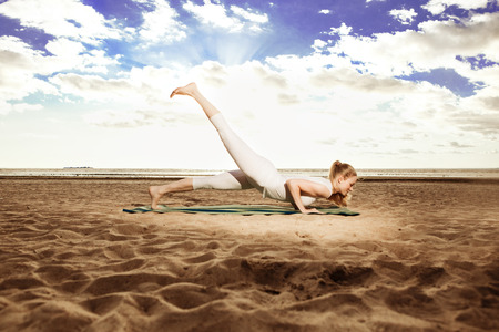 Young beautiful slim woman practices yoga on the beach at sunset. Yoga at sunriseの写真素材