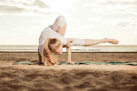 Young beautiful slim woman practices yoga on the beach at sunrise. Yoga at sunset