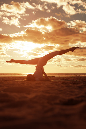 Young beautiful slim woman silhouette practices yoga on the beach at sunset. Yoga at sunrise