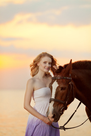Beautiful woman riding a horse at sunset on the beach. Young beauty girl with a horse in the rays of the sun by the sea.の写真素材
