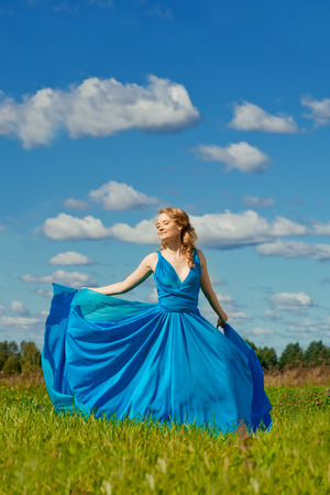 Luxury beautiful woman in long blue evening fashionable dress outdoors. In the sunlight on a green field.の写真素材