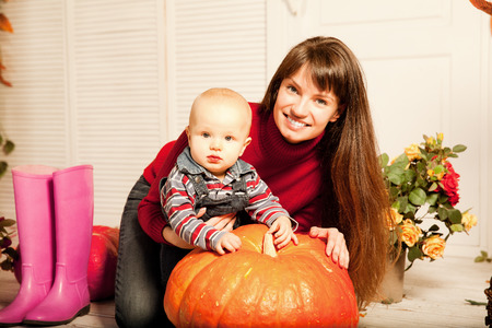 Beautiful young woman with a child on the front porch with pumpkins autumn. Smiling mother and son.の写真素材