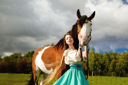 Beautiful young woman with a horse in the field. Girl on a farm with animal. Luxury woman outdoorsの写真素材
