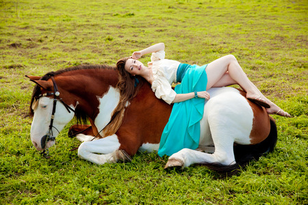 Beautiful young woman with a horse in the field. Girl on a farm with animal. Luxury woman outdoorsの写真素材