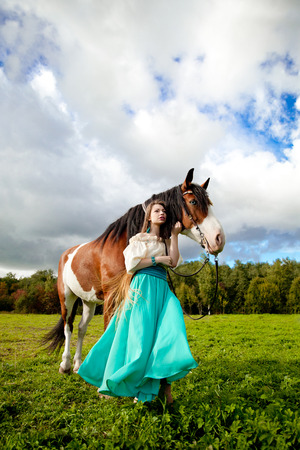 Beautiful young woman with a horse in the field. Girl on a farm with animal. Luxury woman outdoorsの写真素材