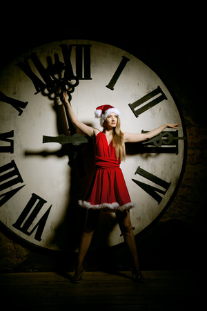 Trendy young woman in Santa costume on the big dial. Girl and clock in Christmas. New Year watchの写真素材