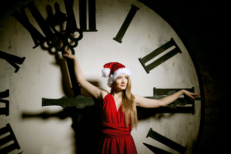 Trendy young woman in Santa costume on the big dial. Girl and clock in Christmas. New Year watchの写真素材