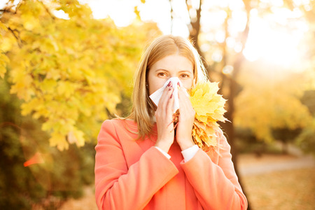 Girl with cold rhinitis on autumn background. の写真素材