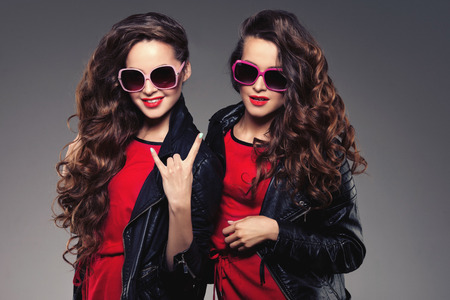 Sisters twins in hipster sun glasses laughing. Two fashion models. Women smiling and positive. Friends group having fun and talking. Youthful, friendship and youth adults people culture concept. Young girls rock partyの写真素材