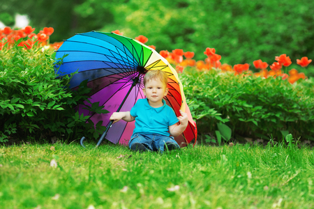 baby with rainbow umbrella in park.の写真素材