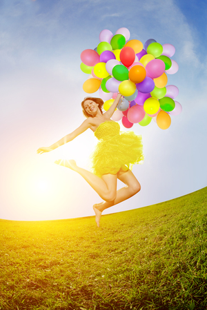 Happy birthday woman against the sky with rainbow-colored air balloons in hands.の写真素材
