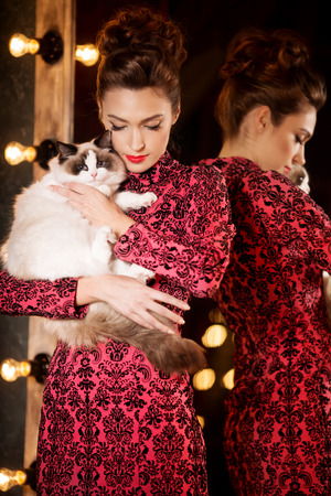 Young beautiful girl near the mirror in a nightclub holding a catの写真素材