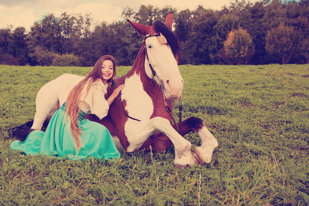 Beautiful young woman with a horse in the field. Girl on a farm with animal. Luxury woman outdoorsの写真素材