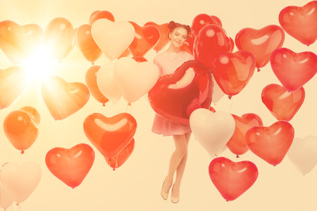 Beautiful girl, stylish fashion model with balloons in the shape of a heart. Woman on Valentine's Day. Symbol of love.の写真素材