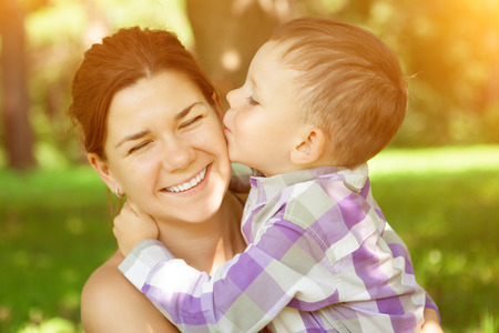 Mom and son. Child kisses his mother on nature background. Positive  summertime scene of love and tenderness. Mummy and baby in parkの写真素材