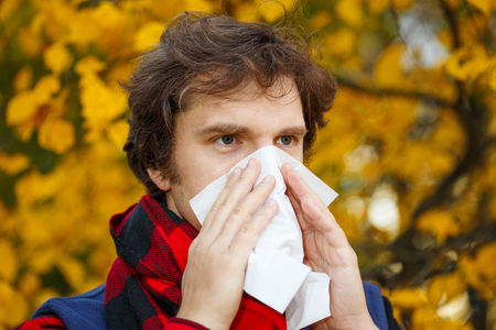 Man with cold rhinitis on autumn background. Fall flu season. Ill sick sneezing male. Handkerchief, vaccine against influenza virus Caught Cold Headache Allergy runny noseの写真素材