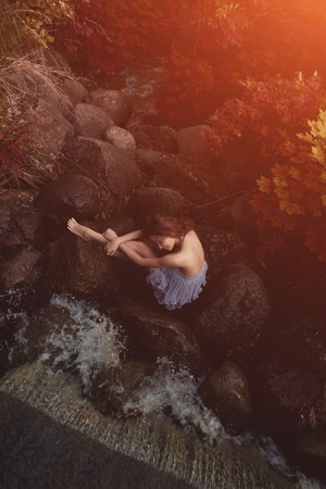 Beautiful woman in fairy forest near a stream. Girl model in the forest, among the grass and leaves near the water.の写真素材