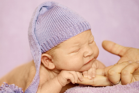 Little newborn baby in a funny hat sleeping in white blanket, lying on bed.の写真素材