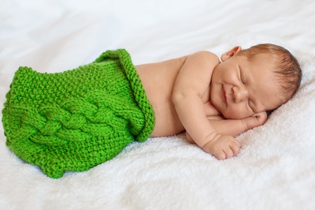 Laughing, smiling  little newborn baby boy sleeping in white blanket, lying on bed.の写真素材