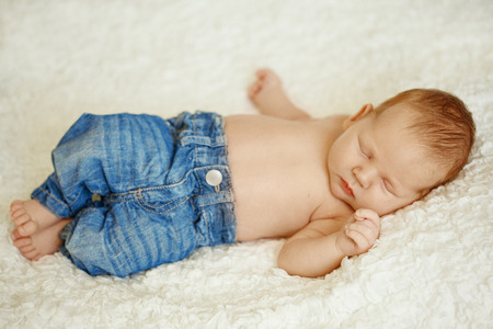 Fashionable newborn baby in jeans sleeping in bed. Fashion for children.の写真素材