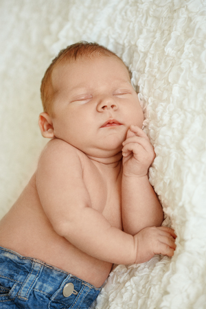 Fashionable newborn baby in jeans sleeping in bed. Fashion for children.の写真素材