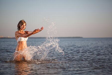 Woman enjoys on beach. Girl jumps on  waves and laughs. Model in swimsuit on  ocean vacation. Tourism and restの写真素材