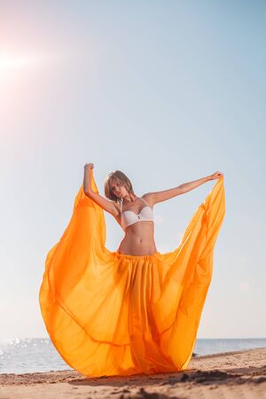 Girl in long dress on beach by sea. Woman with a long cloth near water. Model in a bright long skirt on vacation by  ocean.の写真素材