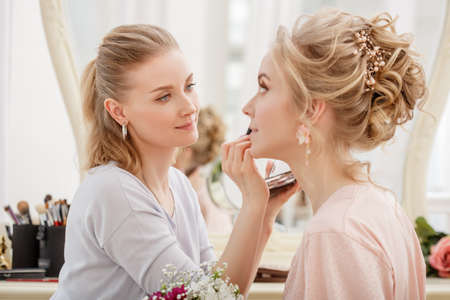 Makeup artist, hair professional stylist makes young beautiful bride bridal makeup before wedding in a morningの写真素材