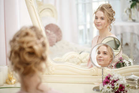 Makeup artist, hair professional stylist makes young beautiful bride bridal makeup before wedding in...