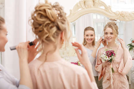 Makeup artist, hair professional stylist makes young beautiful bride bridal makeup before wedding in a morningの写真素材