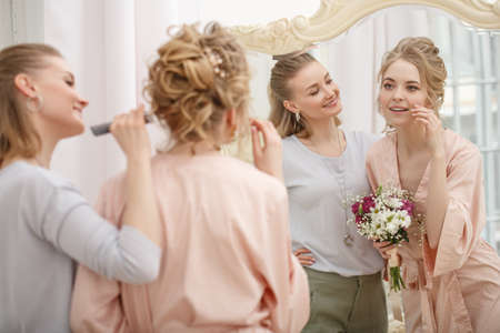 Makeup artist, hair professional stylist makes young beautiful bride bridal makeup before wedding in a morningの写真素材