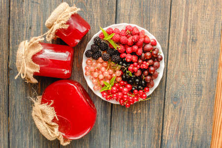 Assorted fresh summer berries and jam in jars. Raspberries, gooseberries, blackberries, currants, wild strawberries, strawberries.の写真素材