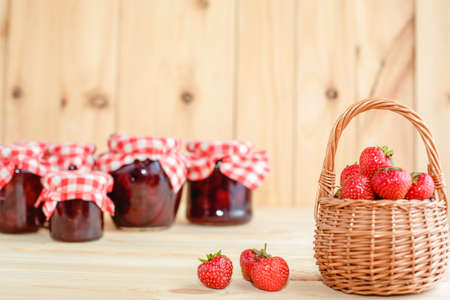 Strawberry jam in a jar on a wooden background with fresh strawberries in a basket.の写真素材