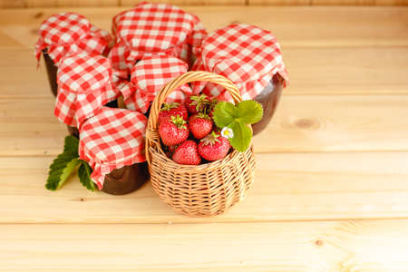 Strawberry jam in a jar on a wooden background with fresh strawberries in a basket.の写真素材
