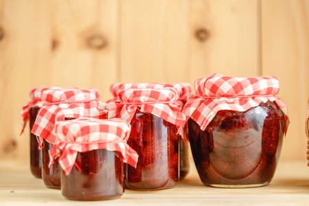 Strawberry jam in a jar on a wooden background with fresh strawberries in a basket.の写真素材
