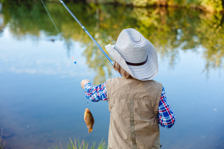 Child is fishing. Boy is a fisherman. Child with a fishing rod caught a fish in a pond. Nice catch!の写真素材