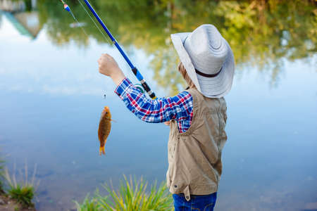 Child is fishing. Boy is a fisherman. Child with a fishing rod caught a fish in a pond. Nice catch!の写真素材