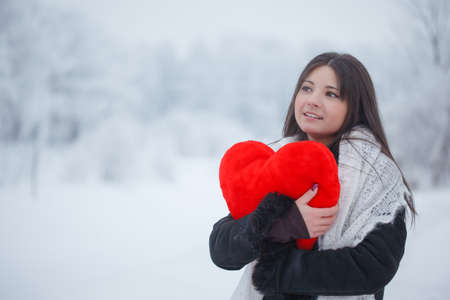 Beautiful girl with a red heart on the street in winter. Valentine's day February 14th. Woman...
