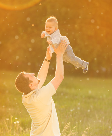 Baby with his father on the background of the sunset in spring. Family playing on a walk in summertime. Kid is happy.の写真素材