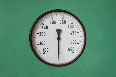 Round industrial thermometer on a machine green background