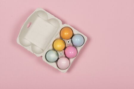 Easter background with a carton egg box with pastel colored easter eggs in it on a pink backgroundの写真素材
