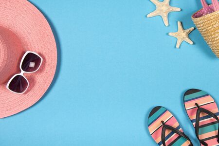 Flat lay with a summer holiday concept with blue background an pink hat, sunglasses, flip flops and beach accessoires seen from a high angleの写真素材