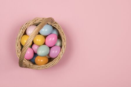 Easter background with pastel colored easter eggs in a basket on a pink background with space for...
