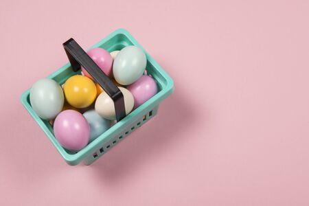 Easter background with pastel colored easter eggs in a shopping basket on a pink background with space for copyの写真素材