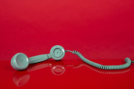 Vintage blue telephone receiver lying on a red backgroundの写真素材