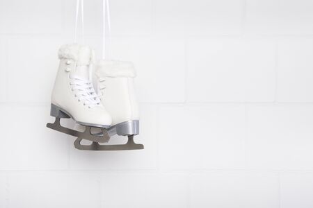 Pair of white figure skates for females hanging at a white concrete background with space for copyの写真素材