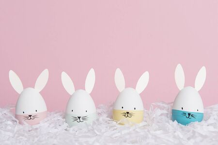 Easter eggs with bunny faces in nest on a pink background with space for copy