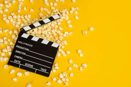 Movie clapperboard and popcorn on a yellow background as a concept for movies with space for copyの写真素材