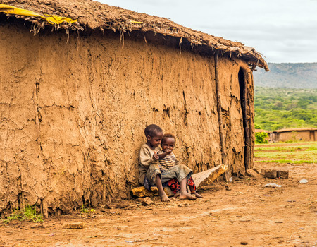 MAASAI MARA, KENYA - OCTOBER 17, 2014 : Two african boys sitting in front of a Masai tribe village houseのeditorial素材