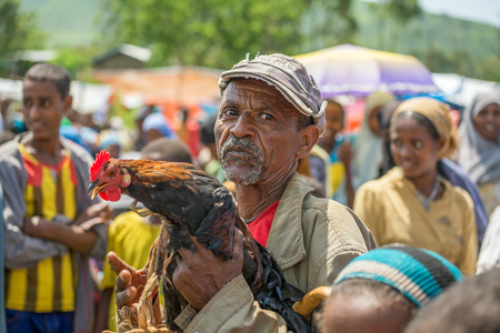 JIMMA, ETHIOPIA - MAY 2, 2015 : Old ethiopian man selling a rooster in a market.のeditorial素材